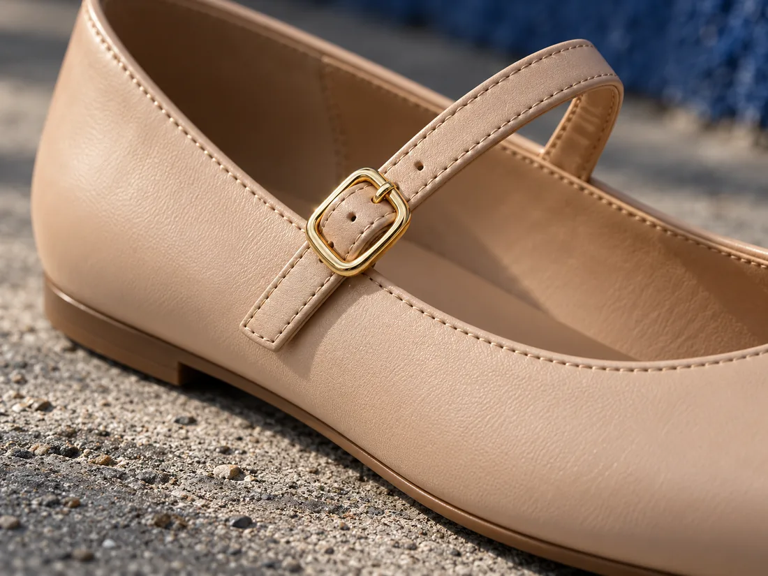 Macro detail of the gold buckle and edge stitching on a nude leather Mary Jane flat